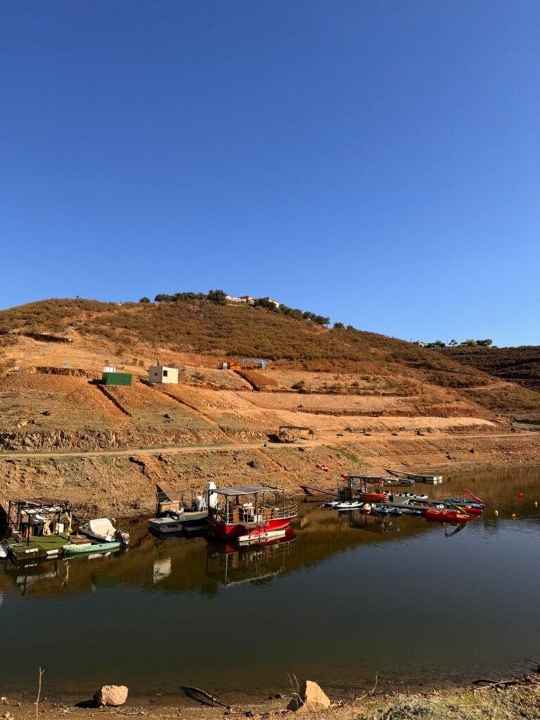 Boats moored on the La Breña reservoir below a red-brown hillside