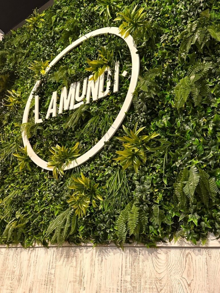 La Mundi logo on a green plant wall above a wooden panel